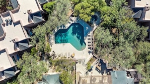 An aerial view of a residential area with a central swimming pool surrounded by trees and houses with sloped roofs.