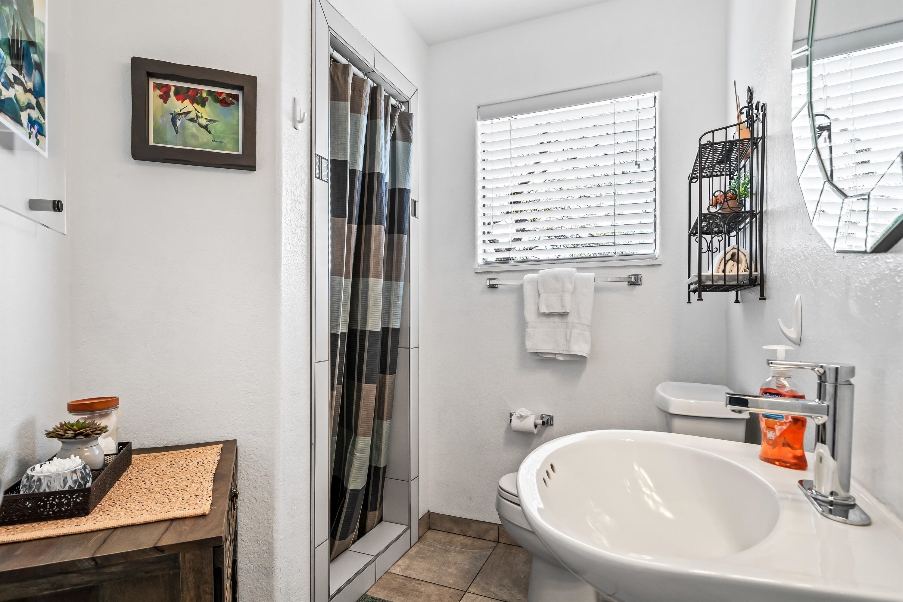 Ein Badezimmer mit Dusche, Toilette, Waschbecken und einem Fenster mit Jalousien.
