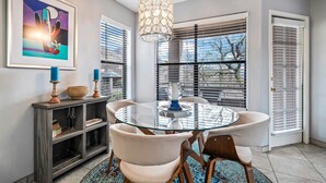 A dining area with a glass table, cushioned chairs, a decorative hanging light, and a framed artwork on the wall.