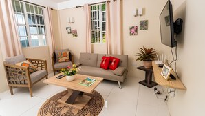 A living room with a sofa, a coffee table with a book, a TV mounted on the wall, and a window with curtains. - Providence,where nature meets home, every path leads to peace.
Strong WIFI, AC. (Mahaut)