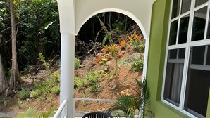 A covered patio with a table and chairs, a potted plant, and a view of a garden with various plants and a small hill. - Providence,where nature meets home, every path leads to peace.
Strong WIFI, AC. (Mahaut)