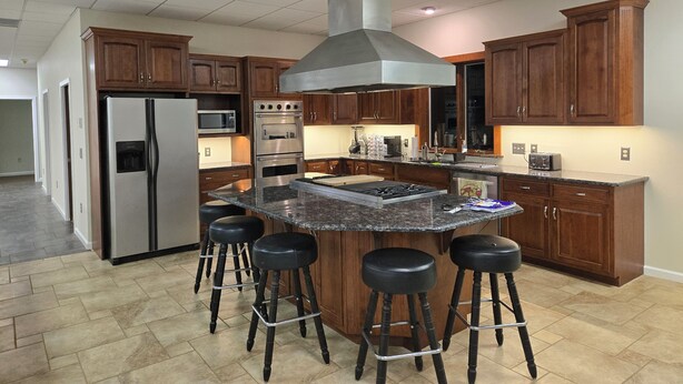 A modern kitchen with a central island, stainless steel appliances, wooden cabinets, and a bar stool seating area. - Spacious House Ideal for Sports Teams, Across from Spooky Nook in Manheim, PA (Manheim)