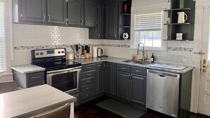 Una cocina moderna con armarios grises oscuros, un refrigerador de acero inoxidable, un horno empotrado y una encimera de granito.