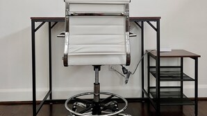 Una silla de oficina moderna con base cromada y asiento blanco, ubicada frente a un escritorio de metal negro con superficie blanca.