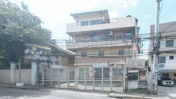 A multi-story building with a gated entrance, a visible balcony on the upper floor, and a parked car in the foreground.