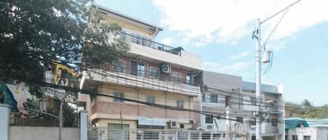 Un edificio de varios pisos con entrada porticada, una escalera y una unidad de aire acondicionado visible.