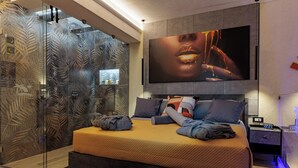 Een moderne slaapkamer met een groot bed, een glazen douche en een flatscreen televisie aan de muur.