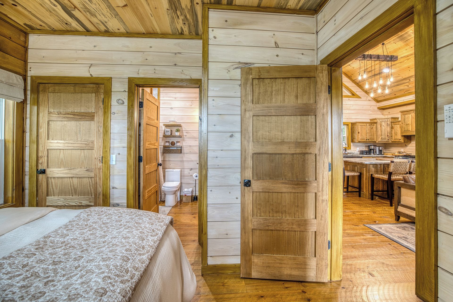 A wooden cabin interior with a bed, a bathroom, and a kitchen area.