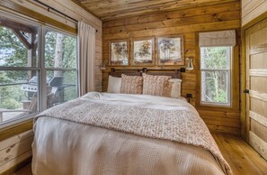 A wooden cabin bedroom with a bed, curtains, and framed artwork on the wall. - New Luxury Cabin in Coosawattee River Resort _ Hot Tub + Views + Sleeps 12 (Ellijay)