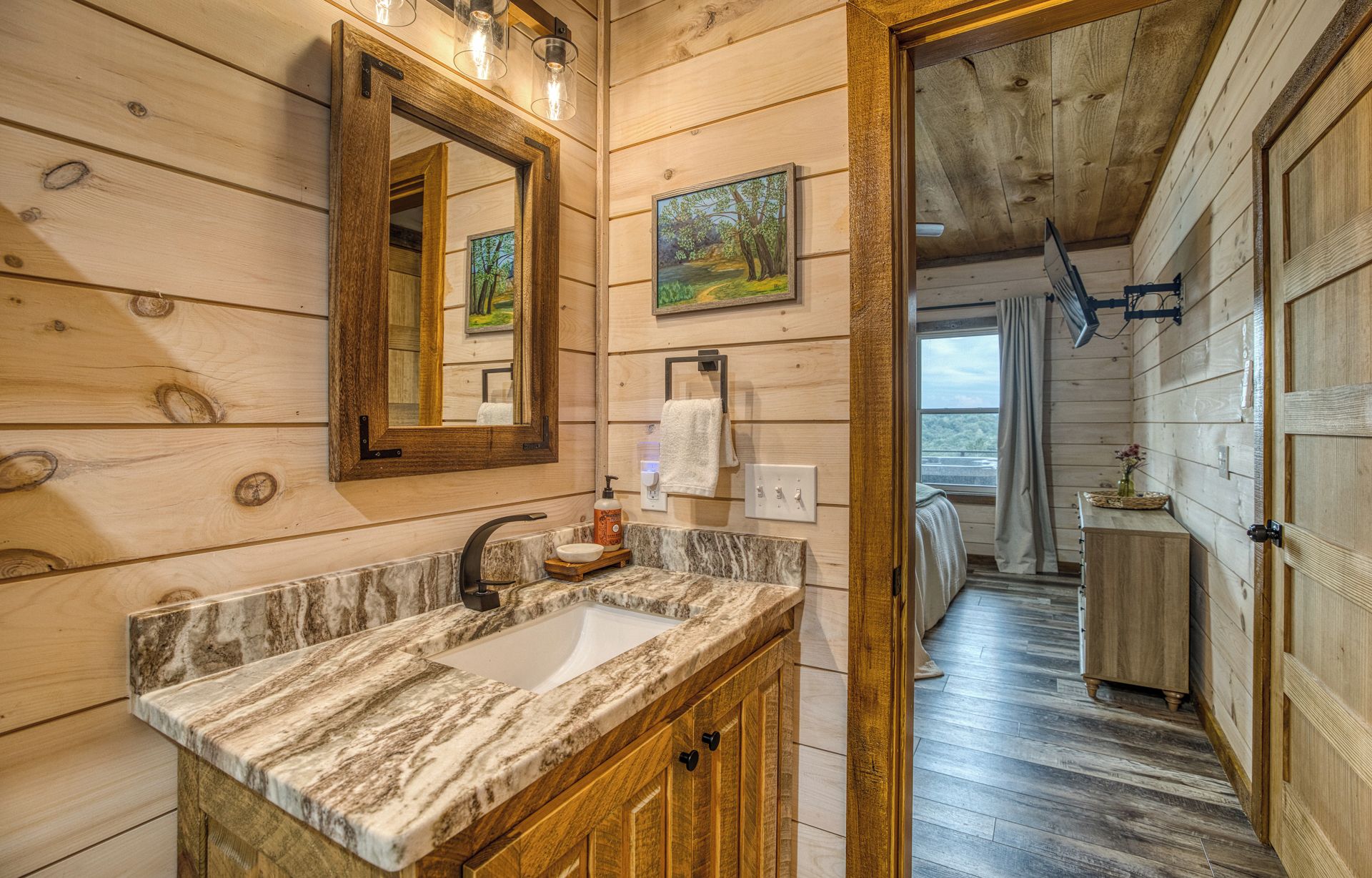 A wooden cabin bathroom with a marble sink, a mirror, and a painting on the wall.