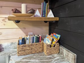 A wooden shelf with books and decorative items, a woven basket with magazines, and a marble countertop. - New Luxury Cabin in Coosawattee River Resort _ Hot Tub + Views + Sleeps 12 (Ellijay)