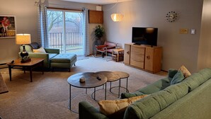 Un salon avec un canapé, une table basse, un téléviseur et une grande fenêtre avec des rideaux.