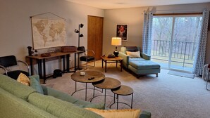 Un salon comprenant un canapé, une table basse, une lampe, une carte accrochée au mur et une vue sur l’extérieur grâce à une grande fenêtre.