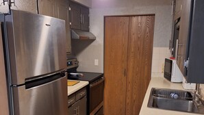 Una cocina compacta con refrigerador de acero inoxidable, armarios de madera, horno empotrado y microondas.