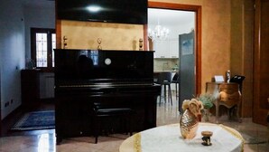 A living room with a black piano, a round table with a vase, and a chandelier. - Versace-Style Villa with Outdoor Spaces and Pool (Borgo Podgora)
