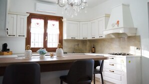 A kitchen with white cabinets, a central island, a chandelier, and a stove. - Versace-Style Villa with Outdoor Spaces and Pool (Borgo Podgora)