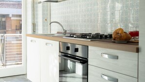 Une cuisine moderne dotée d’une cuisinière en acier inoxydable, d’un four encastré et d’une fenêtre donnant sur un balcon.