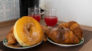 Une table dressée pour le petit-déjeuner, avec un croissant, un beignet et deux verres d’une boisson rouge.
