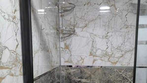 A bathroom with marble walls and a glass shower enclosure.