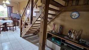A wooden staircase leading to a second floor, a dining area with chairs and a table, and a kitchen area with utensils and a bottle.