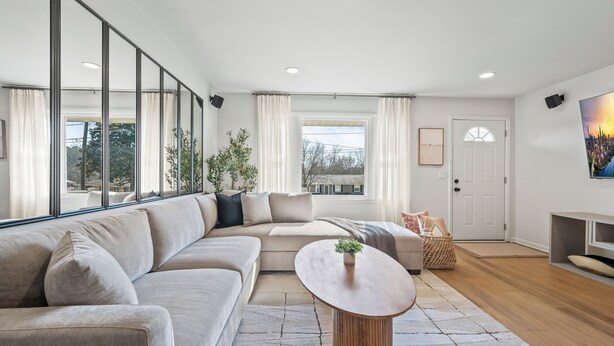 A modern living room with a sectional sofa, a round coffee table, and a view of the outdoors through large windows. - Relaxing Private Ranch Retreat–10 Mins to Downtown. Complete w/ your own Urinal! (Nashville)