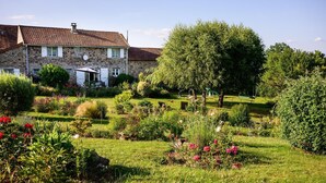 Una casa de piedra con techo de tejas, rodeada de un jardín cuidado con diversas plantas y flores.