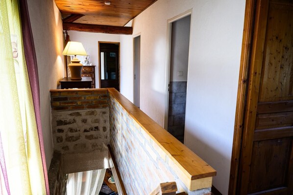 A narrow hallway with a wooden bench, a lamp, and a door leading to another room.