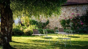 Un jardín con un muro de piedra, una mesa metálica y cuatro sillas metálicas.