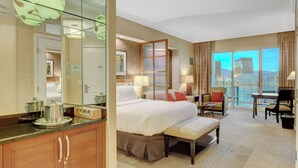 Habitación de hotel con una cama grande, un escritorio, una silla, un banco, un espejo y vistas a la ciudad.