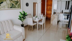 A modern living room with a white sofa, a dining area with a table and chairs, a kitchen with a stove and sink, and a large mirror. - Luxurious & Modern Apartment 1503 Building h2 (Cartagena de Indias)