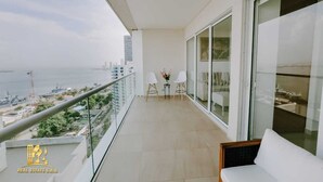 A balcony with a view of the sea and cityscape, two white chairs, and a small table with flowers. - Luxurious & Modern Apartment 1503 Building h2 (Cartagena de Indias)
