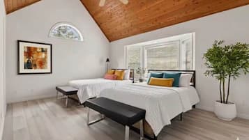 A bedroom with a sloped ceiling, a bed with multiple pillows, a bench, a potted plant, and a framed picture on the wall.