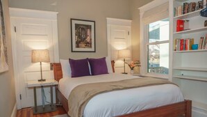 Une chambre à coucher bien rangée, avec un lit, deux tables de chevet dotées de lampes, une bibliothèque et un tableau encadré au mur.