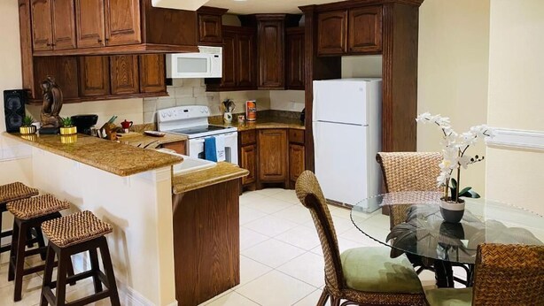 A kitchen with wooden cabinets, a microwave, a refrigerator, a dining table with chairs, and a small island with stools.
