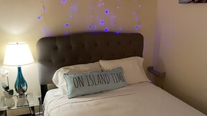 A bedroom with a bed, a nightstand, a lamp, and string lights on the wall.