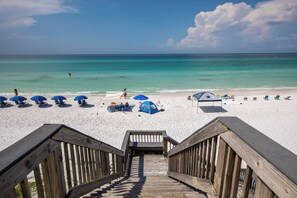 A wooden staircase leading to a beach with white sand, blue umbrellas, and beach chairs. - Blue Mountain Condos #22 (Santa Rosa Beach)