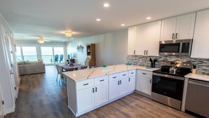 A modern kitchen with white cabinets, a large island, stainless steel appliances, and a dining area with a view. - Blue Mountain Condos #22 (Santa Rosa Beach)