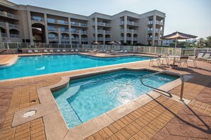 Un espace piscine d’hôtel comprenant une piscine rectangulaire, des chaises longues et un immeuble à plusieurs étages doté de balcons.