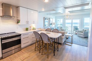 A modern kitchen with white cabinets, stainless steel appliances, and a dining area with wicker chairs and a white table.