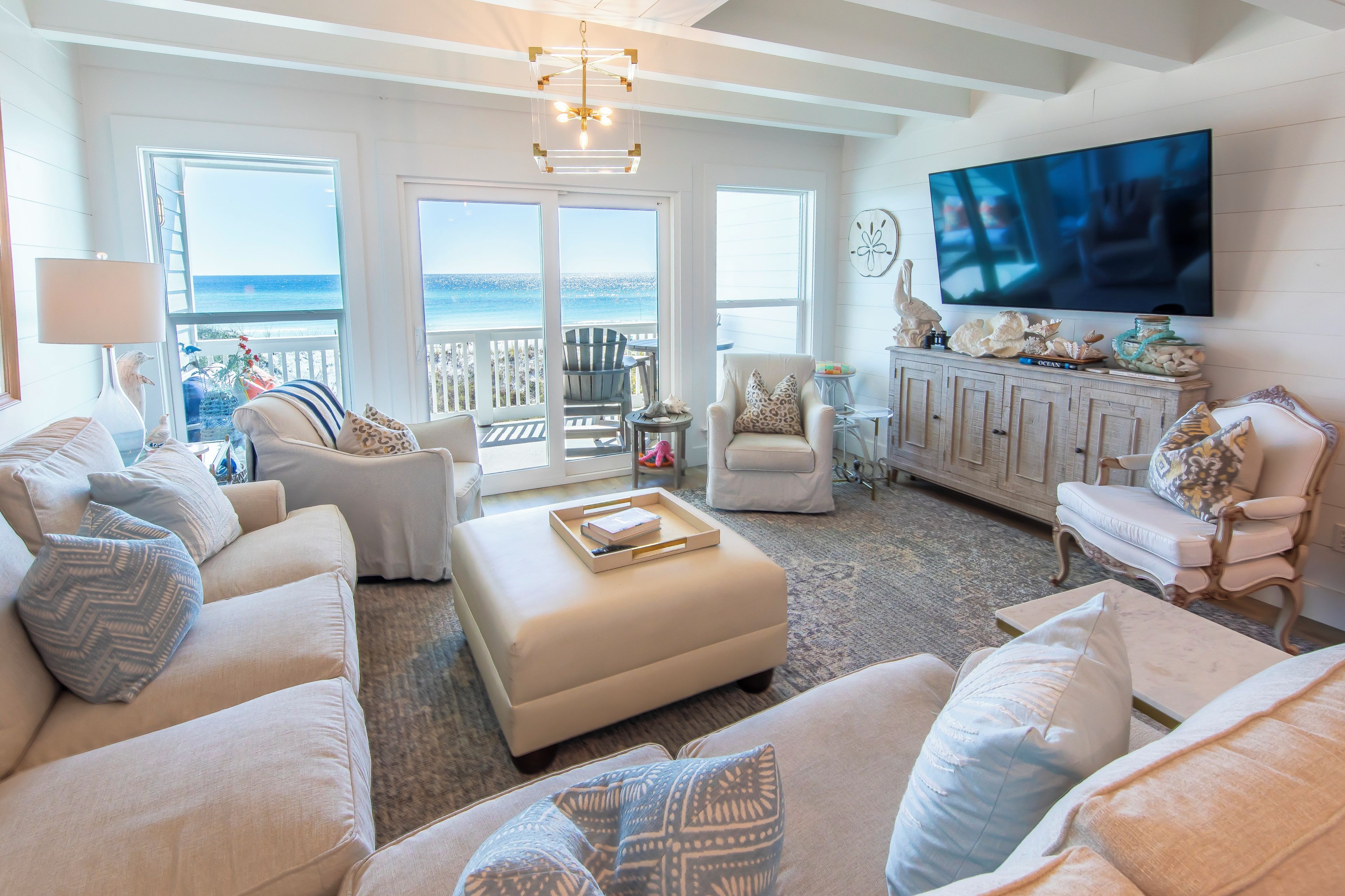 A spacious living room with a large TV, comfortable seating, a view to the ocean, and a balcony.