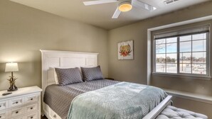 A bedroom with a bed, nightstand, lamp, ceiling fan, window, and artwork.
