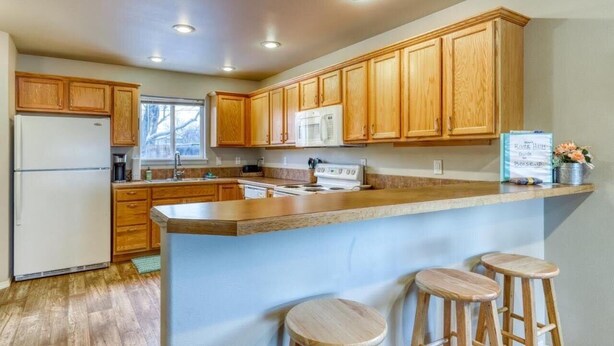 A kitchen with wooden cabinets, a central island with stools, a refrigerator, a stove, and a microwave.