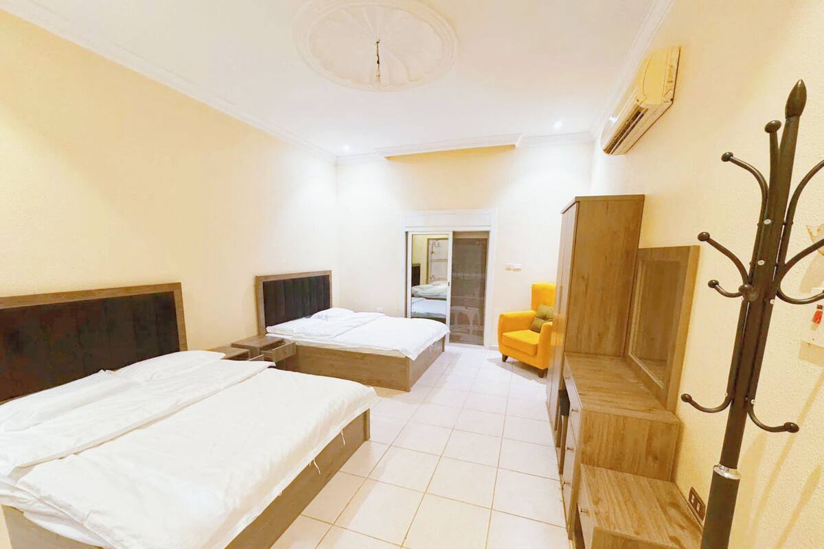 Ein Hotelzimmer mit zwei Betten, einem Fernseher, einem Sessel und einem Kleiderständer.