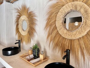 A bathroom with a round sink, a mirror, and decorative wall art. - Sunset hills Apartments (Mazatlán)