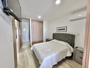 A bedroom with a bed, bedside tables, a wardrobe, and an air conditioning unit. - Sunset hills Apartments (Mazatlán)
