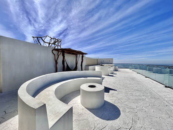 A modern outdoor seating area with a curved bench and a cylindrical planter, overlooking a coastal landscape. - Sunset hills Apartments (Mazatlán)