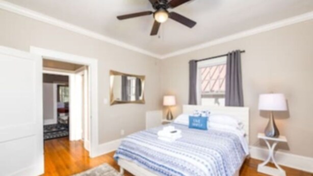 A bedroom with a bed, a ceiling fan, a window with curtains, and a nightstand with a lamp. - The Park Overlook (Charlotte)