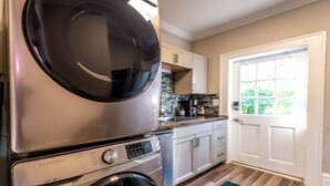 A compact kitchen with a built-in washer and dryer, white cabinets, and a window with a view of greenery. - The Park Overlook (Charlotte)
