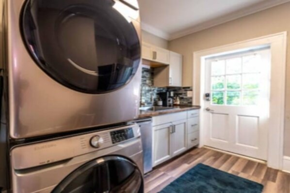 Cocina compacta con lavadora y secadora integradas, armarios blancos y ventana con vistas a zonas verdes.