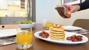 Une table dressée pour le petit-déjeuner, avec des crêpes, des fraises et un verre de jus d’orange.